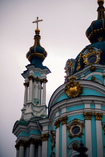 The image features an ornate, baroque-style church with vibrant turquoise and white walls accented by gold decorative details. The domed roof is topped with a cross, and the structure showcases intric