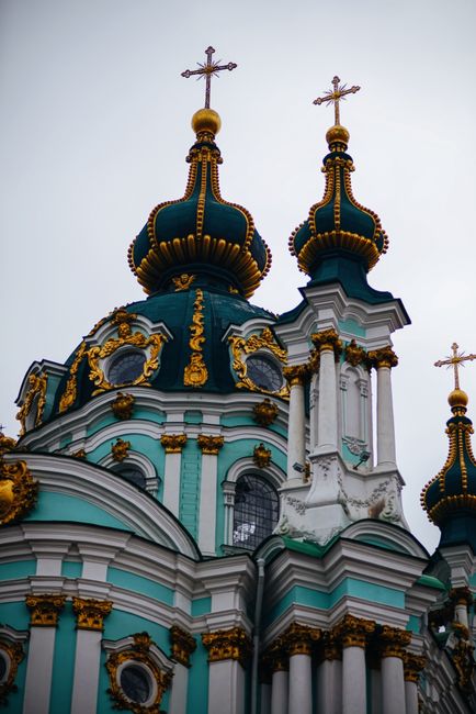 The image depicts the upper section of a historic Orthodox church with ornate domes decorated in vibrant teal and gold, topped with crosses. The domes feature intricate gold detailing along their ridg